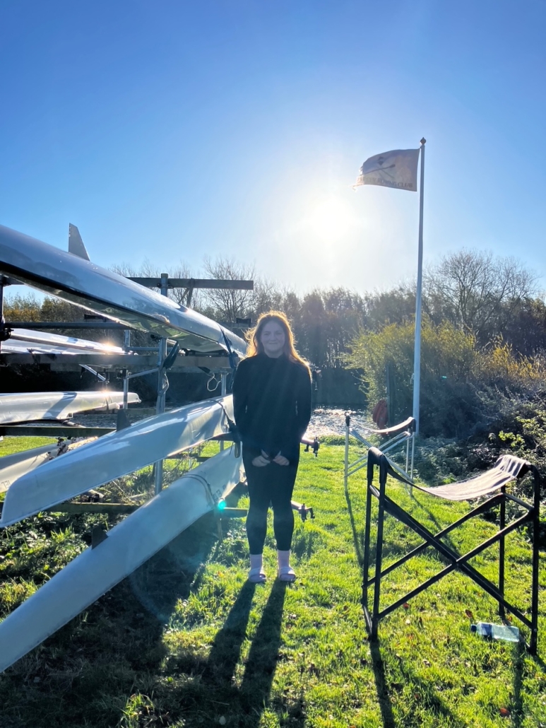 Junior rower standing next to single sculls in the sunshine